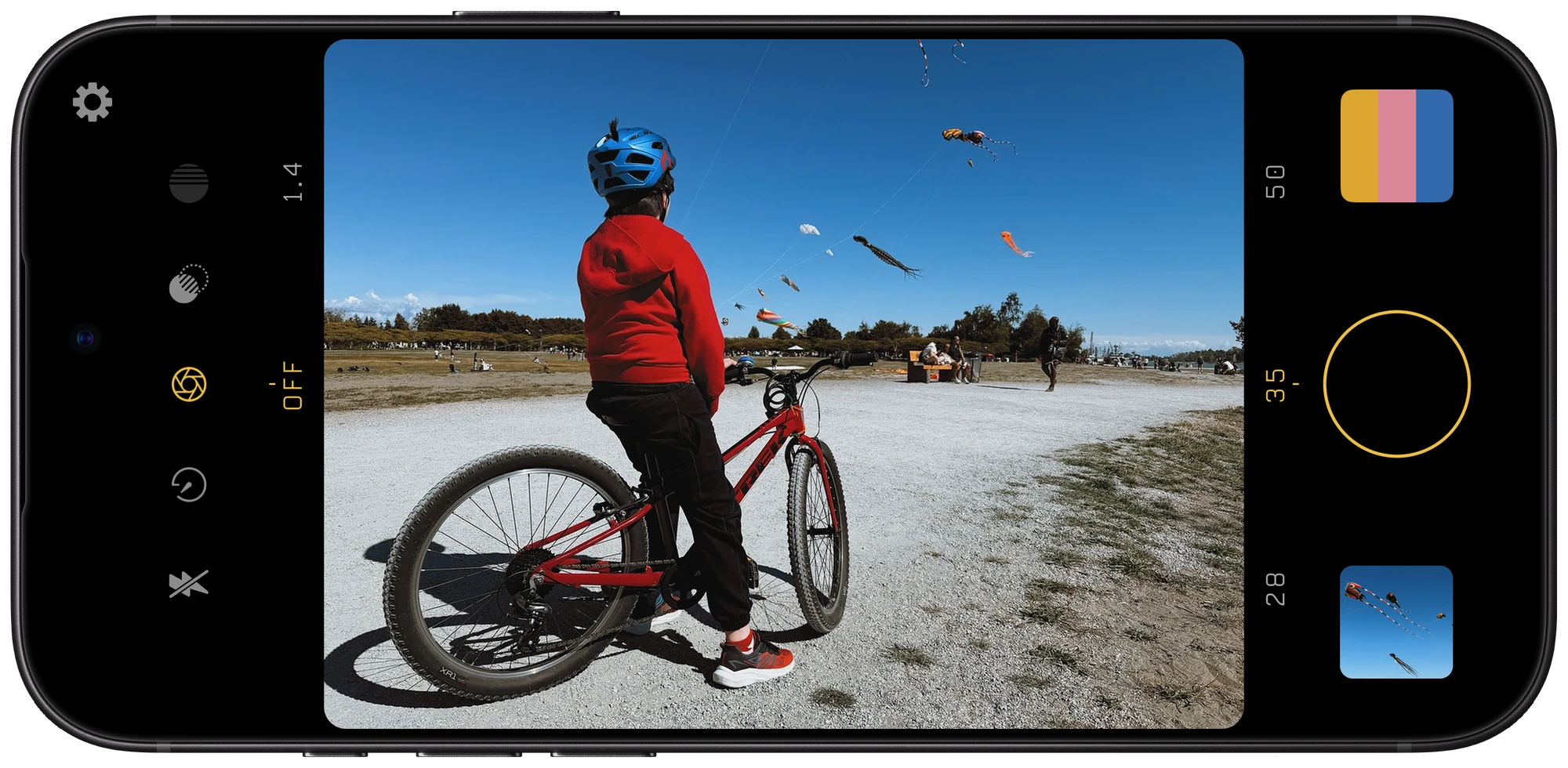 Filmglass on iPhone, framing a child with a bicycle beneath a sky full of kites